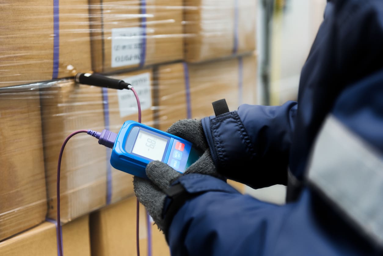 Hand of worker using thermometer to temperature measurement in the goods boxes with ready meals after import in the cold room or warehouse for keep temperature room Temperature controlled medical storage